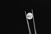 Tweezers holding a shiny diamond on black background. Illustration of the concept of precious stone trading and lab grown diamond