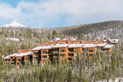 Big Sky, MT, US-January 15, 2022:  Ski condos covered in snow on the side of a mountain surrounded by snow covered pine trees.