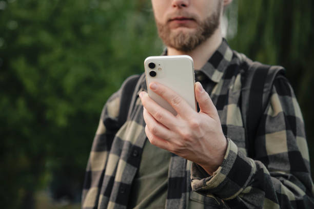 istock Man using white smartphone on blurred nature background, close up. 1706042502