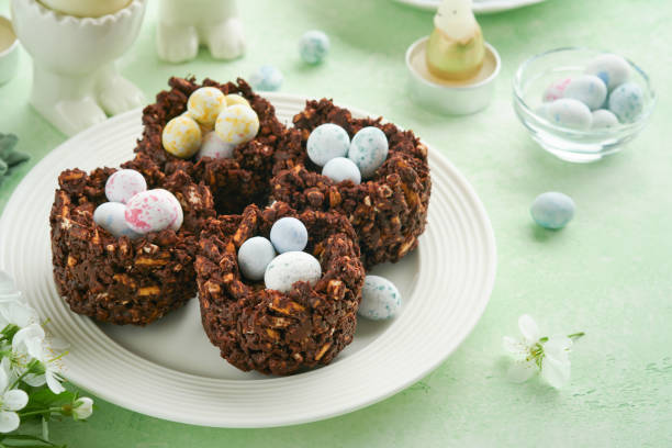 istock Easter chocolate nest cake with mini chocolate candy eggs with blossoming cherry or apple flowers on green background table. Creative recipe for Easter table with holiday decorations. Top view. 1706066026