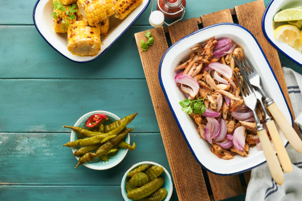 istock Pulled bbq chicken with baked onions on serving platter, bbq corn, pickles, chili peppers and buns for hot dogs and burgers, tomato sauce. Traditional American grilled summer bbq sandwiches dishes. 1706068646