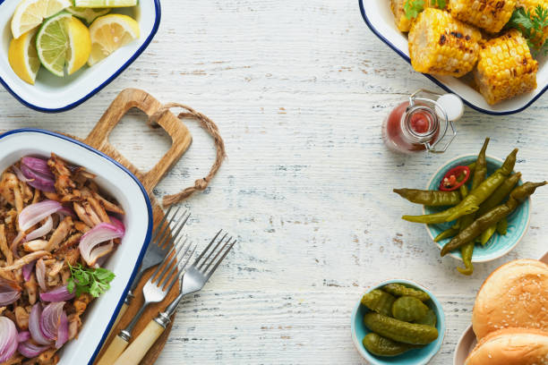 istock Pulled bbq chicken with baked onions on serving platter, bbq corn, pickles, chili peppers and buns for hot dogs and burgers, tomato sauce. Traditional American grilled summer bbq sandwiches dishes. 1706068783