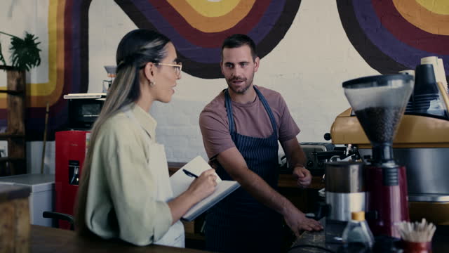 Small business, checklist and employees working in coffee shop planning inventory or stock at a restaurant or cafe. Collaboration, teamwork and owner talking to worker or in discussion about machine