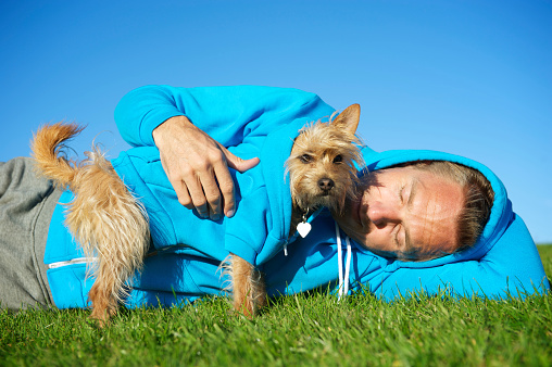 Man relaxes with dog each in matching blue hooded sweatshirts on bright green grass