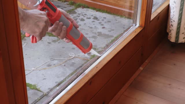 Male hands working with a construction gun, insulating panoramic windows with silicone, close-up