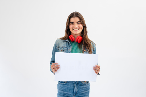 Waist-up studio portrait of a woman looking into the camera with a cheerful expression. She is holding a white sign displaying nothing on it.