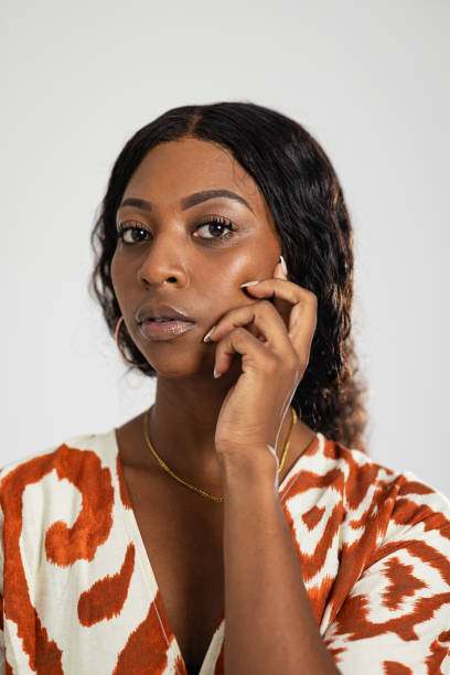 Studio portrait of a female model looking into the camera with a positive expression, showing her teeth. She is wearing a patterned dress and has her hand on her chin.