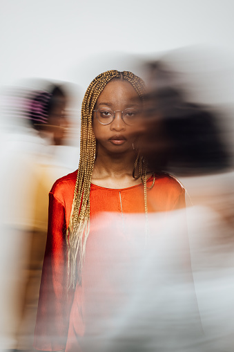 Studio portrait shot of a female model looking into the camera with people walking past her in a motion blur.