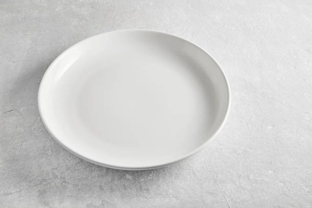 istock Empty white ceramic plate on gray concrete table high angle view. Template for food display and restaurant menu layout 1706147697