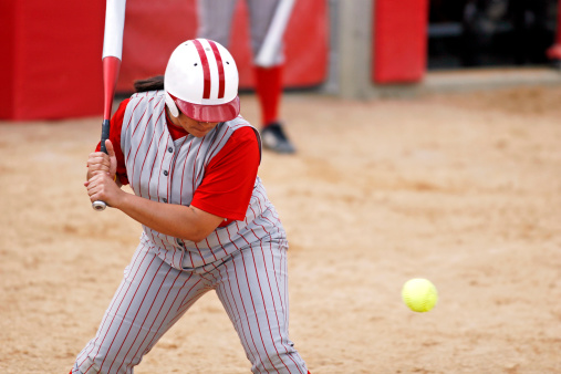 One Sportive Caucasian Female Baseball Player Athlete Tossing Up Ball with Bat wearing Sport Outfit Against Pure White background. Vertical Image