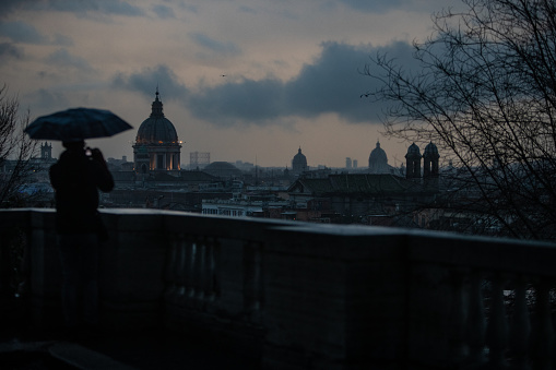 Tourists with umbrellas during a rainy day in Rome, enjoying the view from Pincio to Piazza del Popolo, with domes and cityscape.