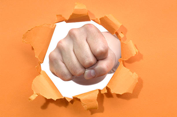 closeup of the fist of a young caucasian man in the air ready to punch or fight, against a graded gray background, with a dramatic effect