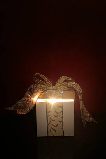 Magical Gift Magical gift sitting on a table with golden bow and light shining out from inside. Soft glow of light against a red wall behind the gift. perfect gift stock pictures, royalty-free photos & images