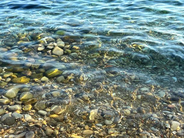 istock Sea shore clear water with smooth pebbles stones 1706160457