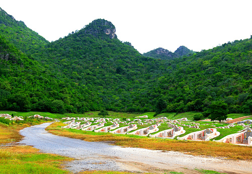 Curve road to Chinese Cemetery for burial of people with green plant and mountain background at Kanchanaburi, Thailand. Sad, lose person, Landmark concept