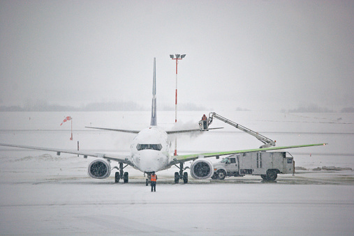 The de-icing of a passenger plane during a snowfall. One wing (green) is completed.