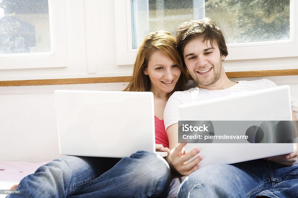 Couple with Laptops - Copy-space Couple sitting on the bed each holding a laptop. Both are looking in the male's computer. Indoor shot on a bright sunny day. Copy-space on the left. Order Stock Photo