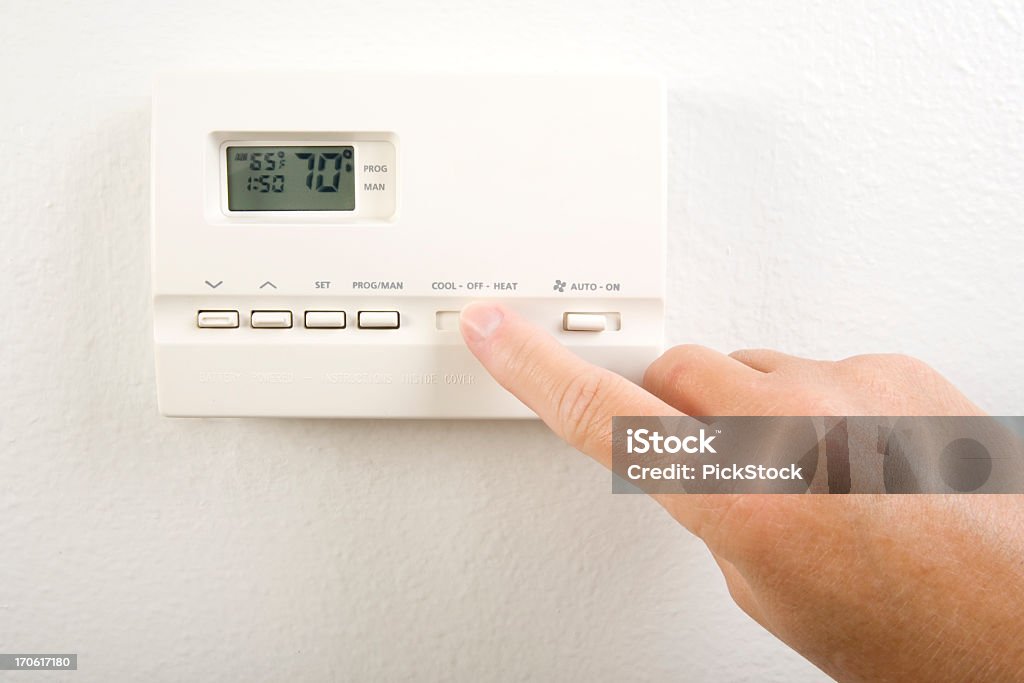 Close-up of hand operating the home heating system controls Setting the Thermostat Thermostat Stock Photo