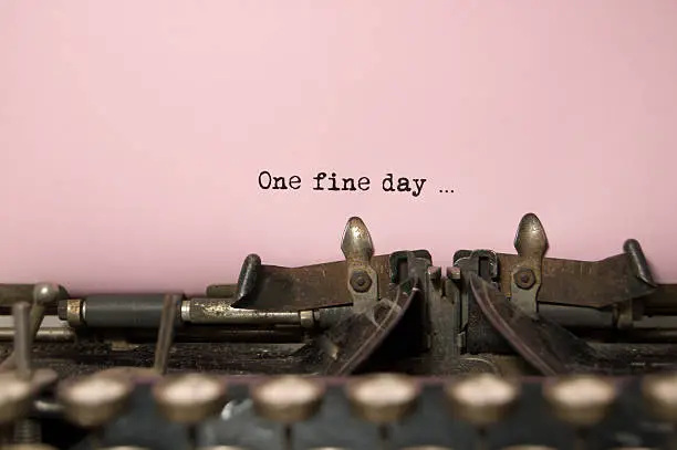 The words - " one fine day " as shown to have been written on a antique typewriter with room for copy.