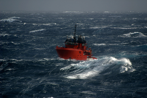 small ship sailing in large waves in a north sea winter storm. Boat is showing rolling motion against horizon in very bad weather. Ship is an oil industry rig support vessel used for offshore safety. Highlights shipping and dangers of sailing and transportation in bad weather and the bravery of the people who do this as a career.