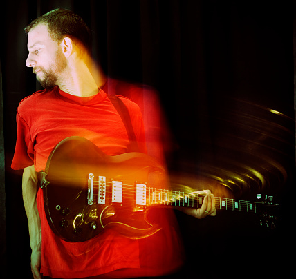 Guitarist lets chord ring out, with intentional motion blur. Cross-processed.
