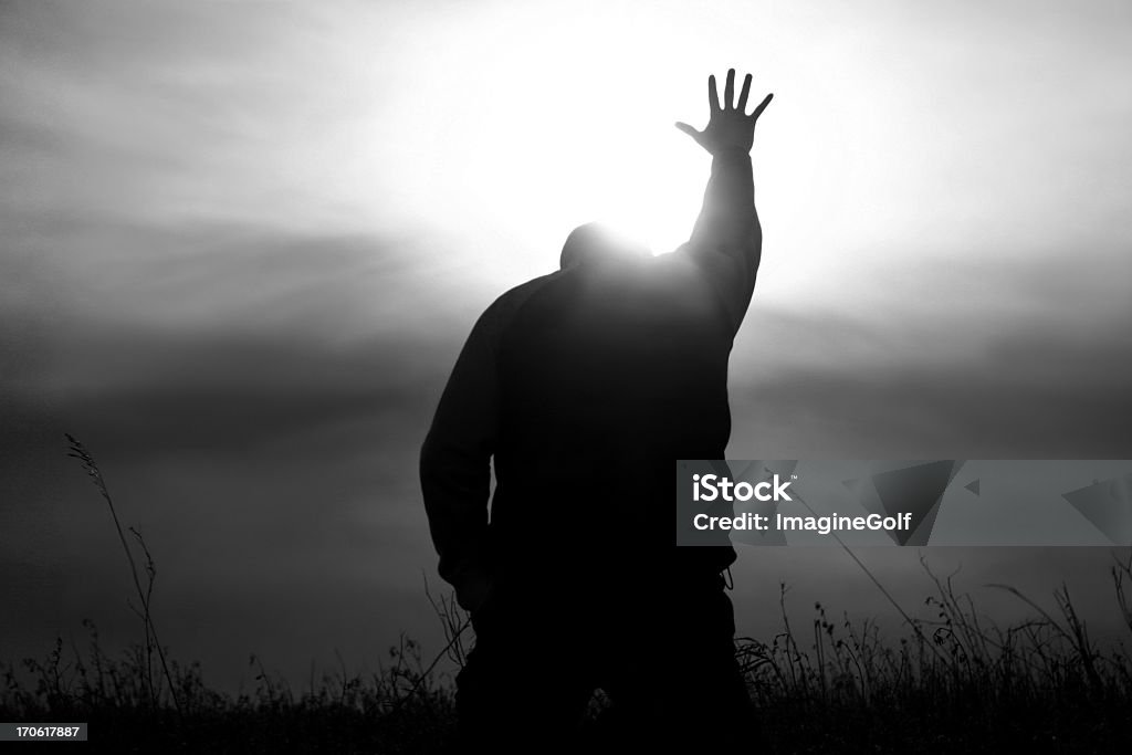 Hand to Heaven in Worship With God Rays A man lifts his hand to heaven in worship. Black and white image depicting a Christian theme with man lifting his hand to heaven in praise. Powerful monochrome image. Additional themes include praise and worship, Christianity, hope, heaven, healing, miracles, salvation, faith, god, prayer, meditation, spirituality, afterlife, and forgiveness.  Praying Stock Photo