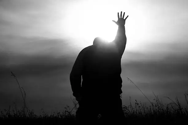 A man lifts his hand to heaven in worship. Black and white image depicting a Christian theme with man lifting his hand to heaven in praise. Powerful monochrome image. Additional themes include praise and worship, Christianity, hope, heaven, healing, miracles, salvation, faith, god, prayer, meditation, spirituality, afterlife, and forgiveness. 