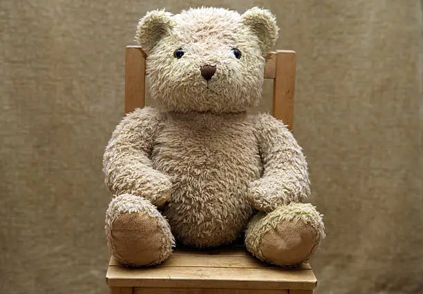 Photo of Old teddy bear sitting on wooden chair