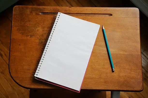 A school chair and desk with paper and pencil.