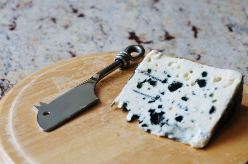 Roquefort, known as 'the king of cheeses' with mouse-shape cheese knife. This blue cheese, made from sheep milk, is in perfect condition, on  a well-used wooden cheese board, which is on a granite surface. True Roquefort comes only from caves in Aveyron, France.