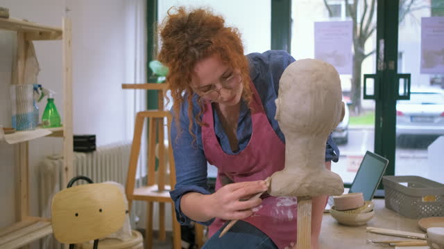 Female sculptor working in pottery studio workshop sculpting human head.