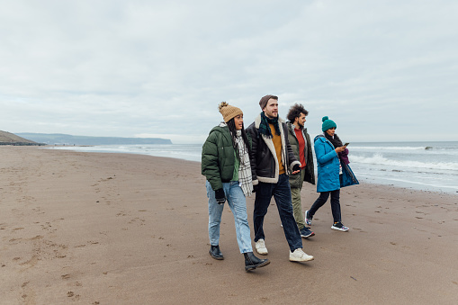 Two mid adult couples enjoying walking along the coast together at the beach. It's cold outside so they are wrapped up in warm clothing in Whitby, North Yorkshire.