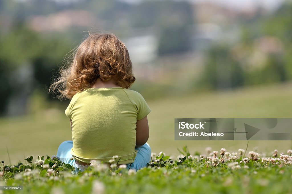 Lone child sitting in field of flowers Solitude moment of a little girl sitting on the floor in grass. Child Stock Photo