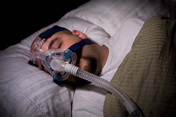Sleep Apnea CPAP Man sleeping while wearing a CPAP mask for sleep apnea. I've been contacted on several occasions about this photo. I guarantee you this is not a picture of you, you husband, your brother, or anyone else but me! This is a photo of me in my bed, with my sheets, my pillow, and my CPAP mask. Again, this photo is a photo of me taken by me. sleep apnea photos stock pictures, royalty-free photos & images