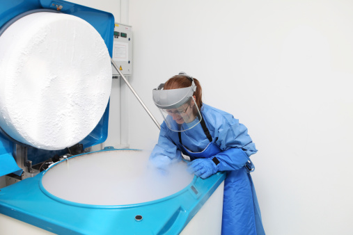 Women doctor in hazmat suit working with container with embryonal cells in liquid nitrogen
