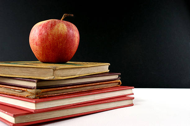 Apple on top of actual school text books from the 1920s and 1930s.  Empty Blackboard in background.  