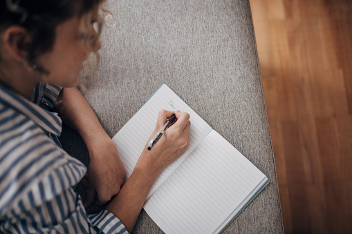 One woman, beautiful young woman writing a diary and relaxing on sofa at home.