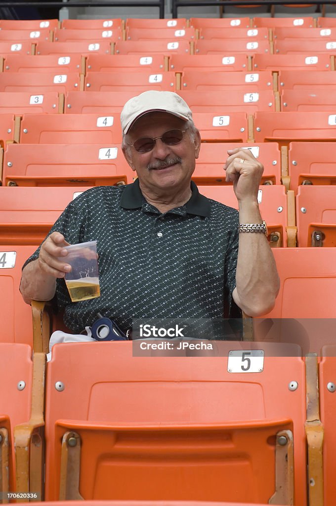 Cheers A senior enjoying his glass of beer at a sports venue. All the orange seats around him are empty. Beer - Alcohol Stock Photo