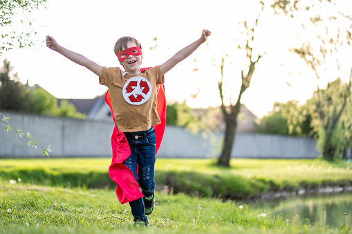 Portrait of a happy boy in nature dressed in a recycling hero costume runing with arms raised