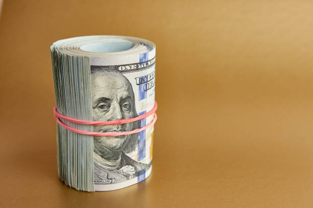 istock Many hundred dollar bills rolled up with a red rubber band on a colored background. 1706230196