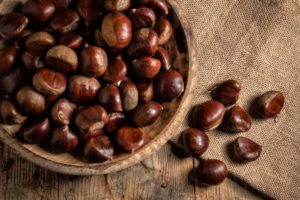 castagne in un piatto di legno su un sacco di tela - chestnut autumn food fruit foto e immagini stock