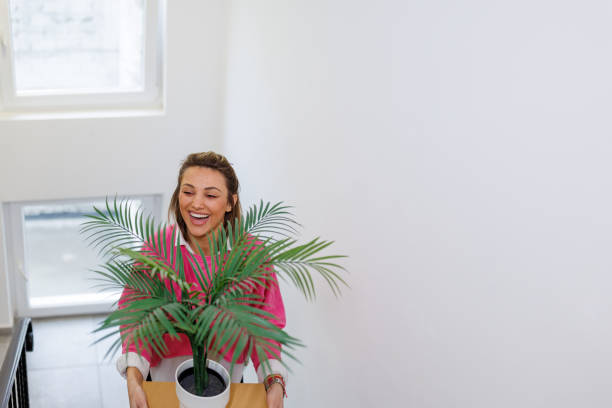 A young woman carefully balances multiple cardboard boxes as she ascends the staircase, clearly in the process of moving into her new apartment