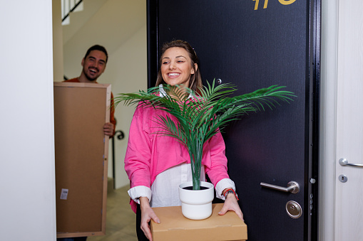 Arms filled with boxes and eyes filled with excitement, a young couple walks into their new apartment, eager to start decorating and making it their own
