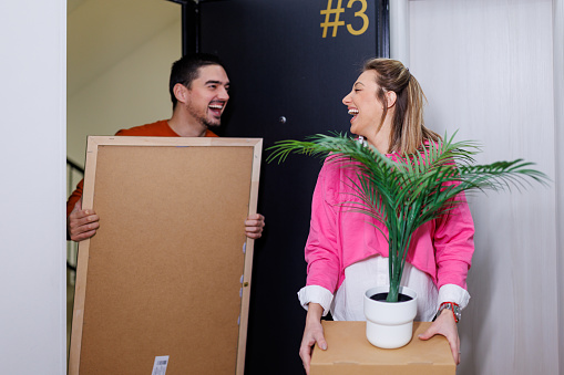 A young couple, balancing boxes and bags, steps into their new apartment with smiles, knowing that this marks the beginning of a new phase in their relationship