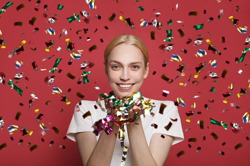 Happy lovely woman on red background with confetti. Happy celebration of New Year or birthday