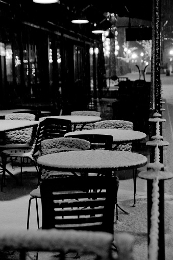 Tables and chairs of a cafe covered with snow during the night in winter.