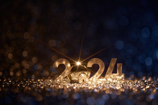 Low key photography of the golden number 2024 and Christmas ornament surrounded by blue and gold sparkling defocused lights. Native image size: 7952x5304