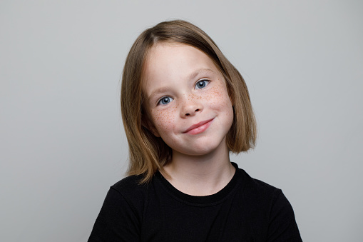 close-up studio portrait of a 9 year old girl with long brown hair in a gray dress on a beige background