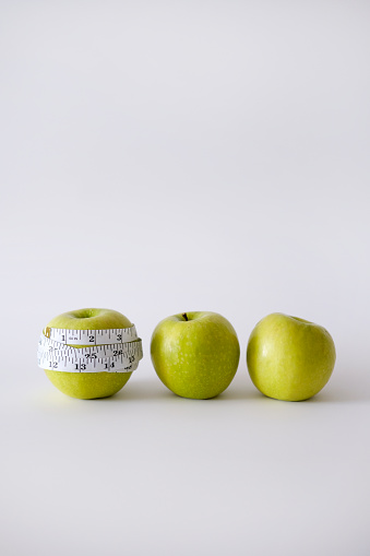 Green apple with white measurement tape. The concept of weight loss and diet. Take care of your body. Foods to eat when losing weight