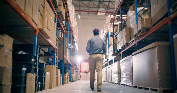 istock Man, back and walking in storage warehouse for manufacturing, distribution and industrial delivery. Factory manager, logistics and check inventory of shipping boxes, stock management and production 1706331212